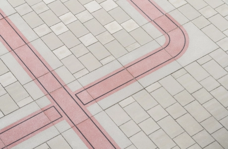 Nahaufnahme einer grau-beigen Pflasterfläche, durch welche sich ein Band aus roten Betonsteinen zieht.