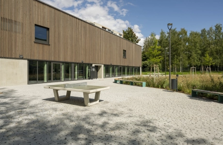 Vorplatz der Grundschule mit natürlichem Ökopflaster GDM.BOLERO stone auf dem eine Tischtennisplatte steht. Im Hintergrund eine natürliche Wiese und ein Wald.