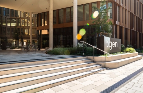 Blick auf eine breite, kalksteinfarbene Treppe aus GDM.MASSIMO step mit schwarzem Kontraststreifen an der Trittkante. Die Treppe führt zu einem großen Bürogebäude. Die 