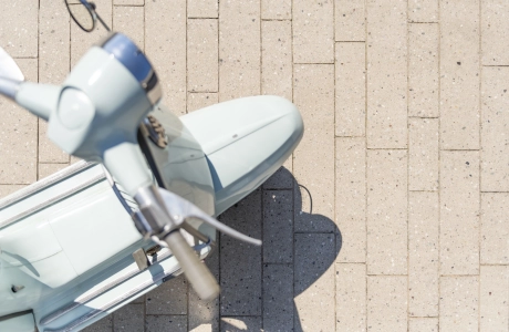 Draufischt auf eine himmelblaue Vespa auf einer geplasterten Fläche mit 
Terrazzo-Steinen mit sichtbarer Körnung Format eines Stabparkets.