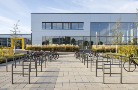 Großer Platz mit vielen Fahrradständern und Fahrrädern. Auf der Fläche ist der versickerungsfähige GDM.SCENIC individual verbaut. Im Hintergrund ist die graue Fassade des Schwimmbades zu sehen. Drumherum sind Gräser, Sträucher und Bäume.
