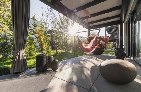 Sonnige Terrasse mit großformatigen Platten und Hängeschaukel.