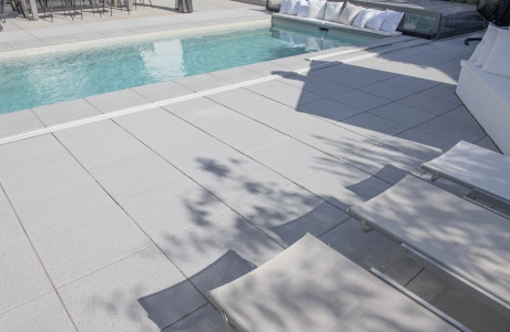 Graue GDM.NUEVA light Platten um einen Pool herum verlegt. Im Vordergrund sind die Fußenden von mehreren Gartenliegen zu erkennen.