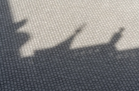 A paved area consisting of anthracite-colored, small-format concrete blocks laid in rows. A building casts a large shadow on the paving.
