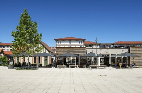 Marktplatz Beelitz-Heilstätten mit großzügiger Platzfläche aus GDM.NUEVA stone Pflastersteinen in der Farbe Sandstein-Uni und gastronomischen Angeboten im Hintergrund.