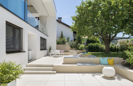 Private modern garden with sandstone-colored terrace and lots of greenery