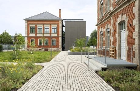 Gebäudeseite der RekoSUN Stadtentwässerung Nürnberg mit Wegen und Platzflächen aus GDM.ACENTRO stone in Granit Perlmut-Gelb.