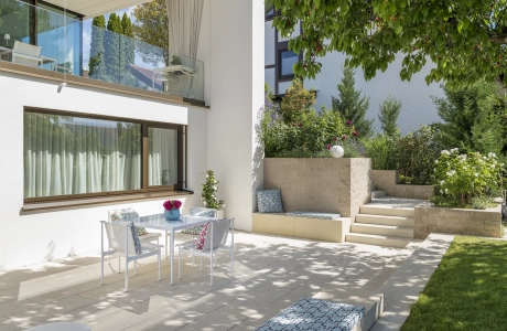 Private modern garden with sandstone-colored terrace and lots of greenery