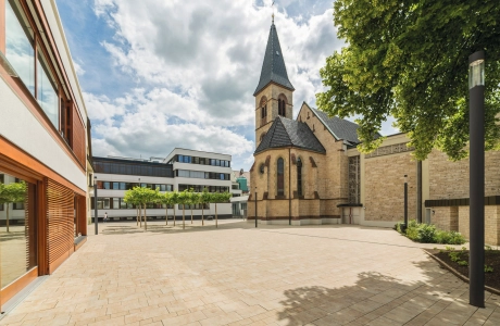 gepflasterter Kirchenvorplatz mit modernen Gebäuden und historischer Kirche