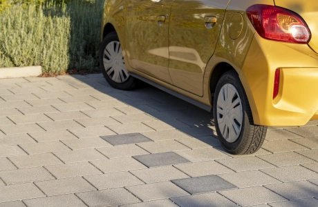 Nahaufnahme einer grauen Parkfläche mit anthrazitfarbenen Steinen zur Abgrenzung der einzelnen Stellplätze. Auf einem der Parkplätz steht ein gelbes Auto.