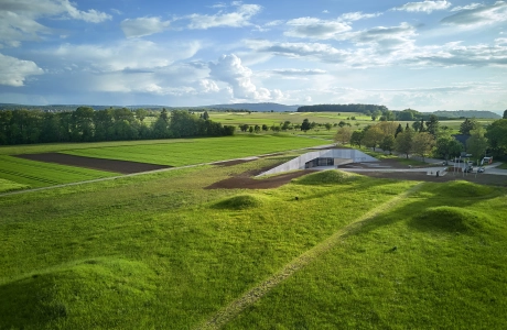 Modernes Gebäude umgeben von grünen Wiesen, Feldern und Bäumen.