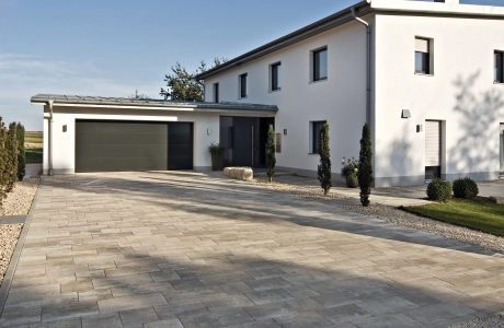 Hofeinfahrt eines Einfamilienhauses mit Garage und Pflanzen auf einem Privatgrundstück.