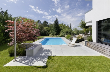 Begrünter Garten mit Pool und großformatigen Terrassenplatten auf einem Privatgrundstück.