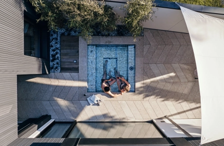 Vogelperspektive auf eine Terrasse in Fischgrätverband. Im kleinen Whirlpool sitzen zwei Menschen. Der Bodenbelag ist GDM.AWA tile von GODELMANN und im Ellbogen bzw. Fischgrätverband verlegt.