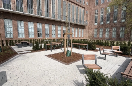 GDM.KLIMASTEIN auf einer großzügigen Platzfläche mit Sitzbänken, Baumstandorten und Aufenthaltsbereichen vor Backsteinfassaden.