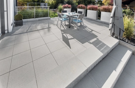 Großflächige Terrasse mit grauen Terrassenplatten und Stufen umgeben von Pflanzgefäßen.