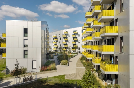 Blick auf eine große Wohnanlage mit mehrgeschossigen Gebäuden. Diese haben eine helle Fassade und auffallend gelbe Balkonbrüstungen. Im Innenhof der Wohnanlage sind der GDM.SCENIC individual und der GDM.SCADA liner verlegt.