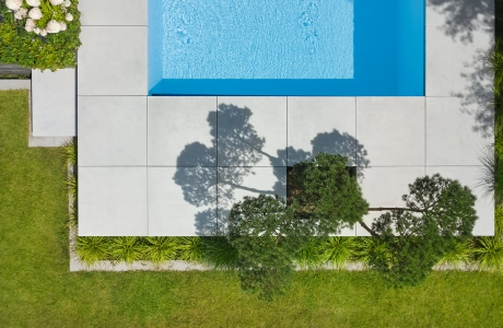 freischwebend und erhöht gesetzte Platten aus Sichtbeton in 100 x 100 cm um einen modernen Pool mit integrierter Bepflanzung.