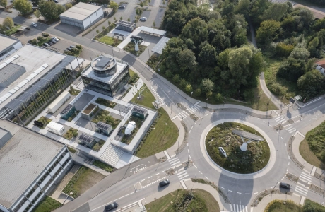 Eine Drohnenaufnahme auf eine moderne Gebäudeanlage, welche an einem großen Kreisverkehr liegt.