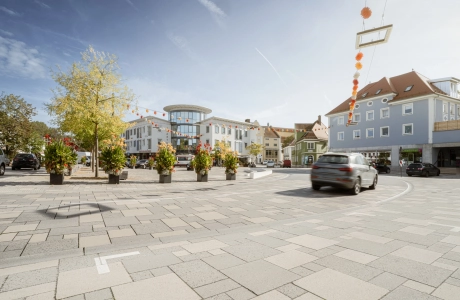 befahrbare Großfromatplatten im wilden Verband und abgestuften Grautönen auf einem Stadtplatz mit Bepflanzung.