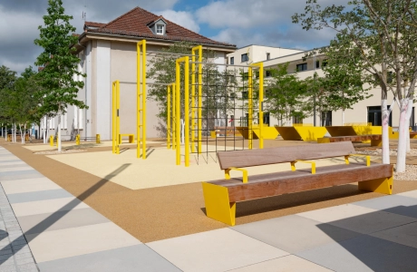 GDM.SCENIC individual auf einer großzügigen Platzfläche mit gelben Sitzbänken, Kletterelementen und jungen Bäumen.