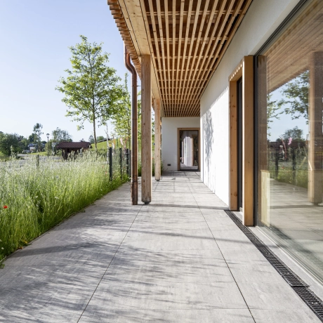 Großformatige Platten als Terrassenbelag vor einer begrünten Wiese.