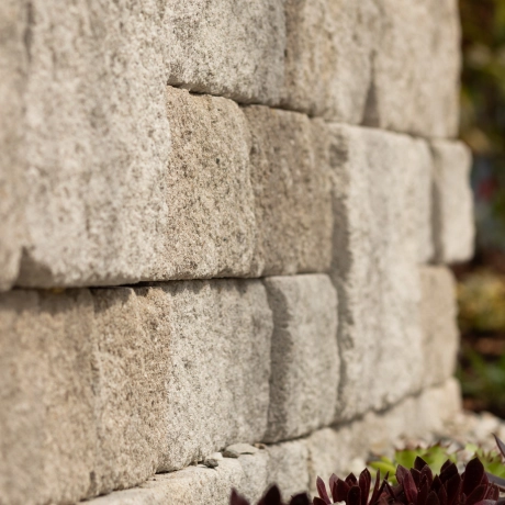 Close-up of a machine-aged wall in front of a flower bed.