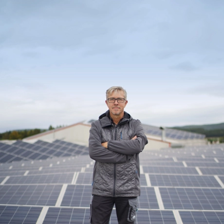 Ein GODELMANN Mitarbeiter steht auf dem Dach einer Halle mit verschränkten Armen. Vor und Hinter ihm sind PV-Anlagen zu sehen, die gesamten Dachflächen sind mit Photovoltaik ausgestattet.