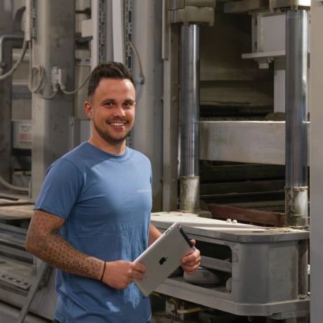 Plant and machine operator stands in front of a production plant holding an iPad.