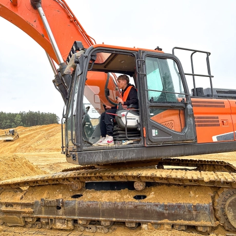 Junge sitzt auf Bagger, im Hintergrund ist die Sandgrube zu sehen.