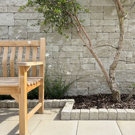 Wooden bench in front of a privacy wall with framed bed and patio slabs.