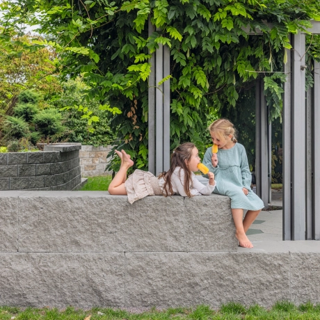 Zwei Mädchen sitzen auf der Schwerlastmauer GDM.MAXI block mit bruchrauen Sichtflächen