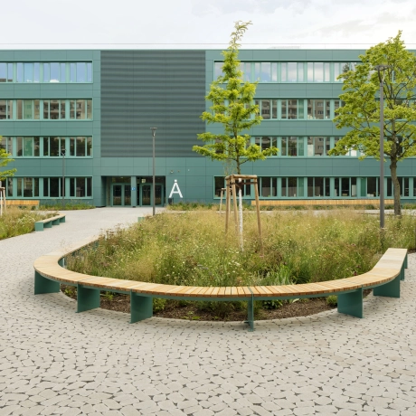 Vorplatz Schulgebäude mit grünen Flächen und Gehweg mit Pflasterung: der Flächenbelag GDM.BOLERO stone ist versickerungsfähig, begrünbar und durch seine organische runde Form besonders in der Flächengestaltung