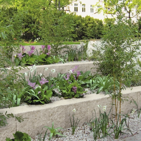 Ein Garten mit Pflanzen und Bäumen, umgeben von einer steinernen Mauer, die eine ruhige Atmosphäre schafft.