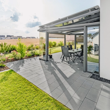 Terrasse mit Wintergarten und rechteckigen Terrassenplatten in Grau-Anthrazit. 