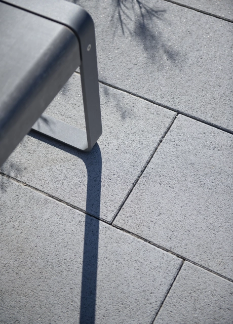 Nahaufnahme des grauen GDM.NUEVA stone neben dem Gestell einer modernen Metallbank.