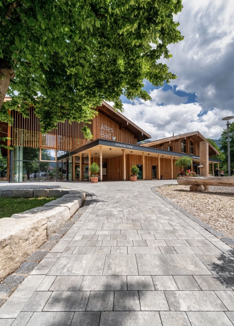 Modern gepflasterter Weg zu Bürgerzentrum mit angrenzender erhöhter, von Mauersteinen umfasster Grünfläche 