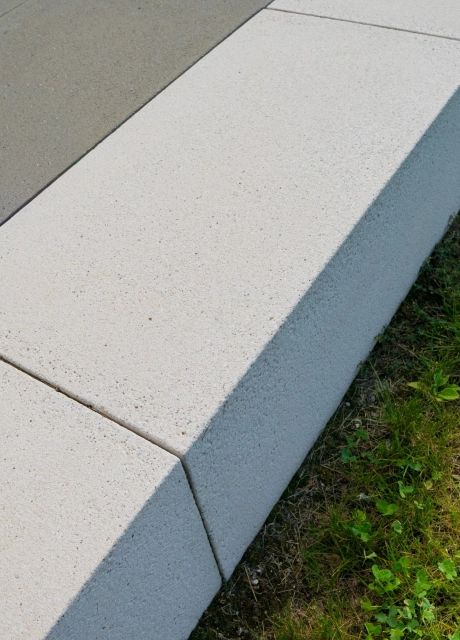 Nahaufnahme eines hellen GDM.SCENIC seat als Sitzkante entlang einer anthrazitfarbenen, gepflasterten Fläche, mit klarer Linienführung und angrenzender Grünfläche.