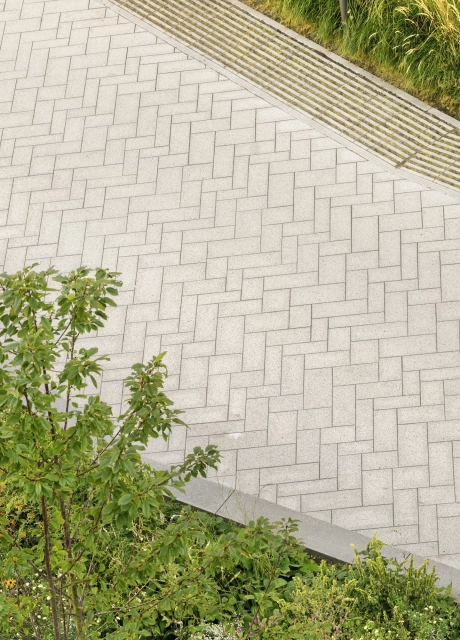 Nahaufnahme eines gepflasterten, basalt- und granitfarbenen Weges mit GDM.SCENIC individual. Am Rand ist auch der graue GDM.SCADA liner sowie grün bepflanzte Beete zu finden.