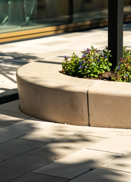 Nahaufnahme des kalksteinfarbenem GDM.MASSIMO seat. Dieser dient hier als Einfassung für ein begrüntes BeetDavor ist der GDM.SCENIC individual in verschiedenen Kalksteinfarbtönen verlegt. 