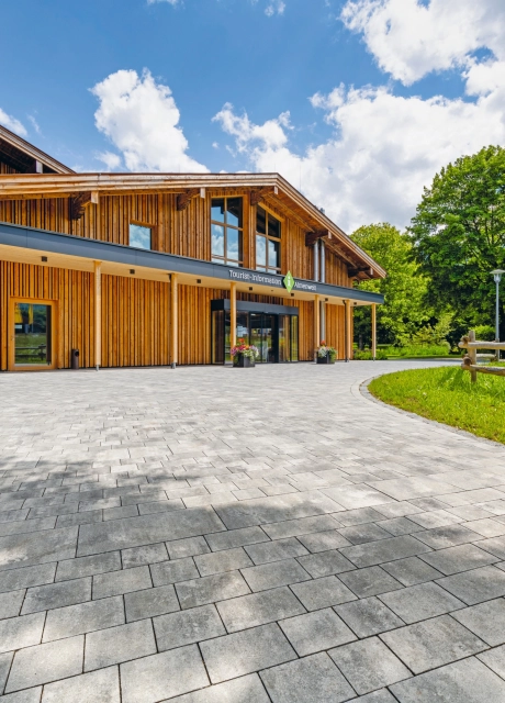Modern gepflasterter Platz mit großer Grünfläche, Bäumen vor einem Bürgerzentrum  mit Holzfassade