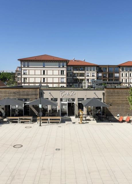 Marktplatz Beelitz-Heilstätten mit großzügiger Platzfläche aus GDM.NUEVA stone Pflastersteinen in der Farbe Sandstein-Uni und gastronomischen Angeboten im Hintergrund.