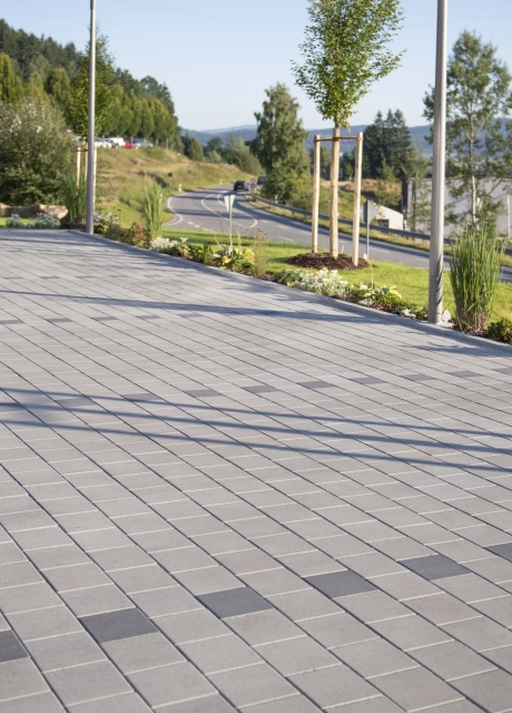 Grau gepflasterte und versickerungsfähige Parkfläche mit dunkelgrauem Pflaster zur Abtrennung der einzelnen Parkplätze.