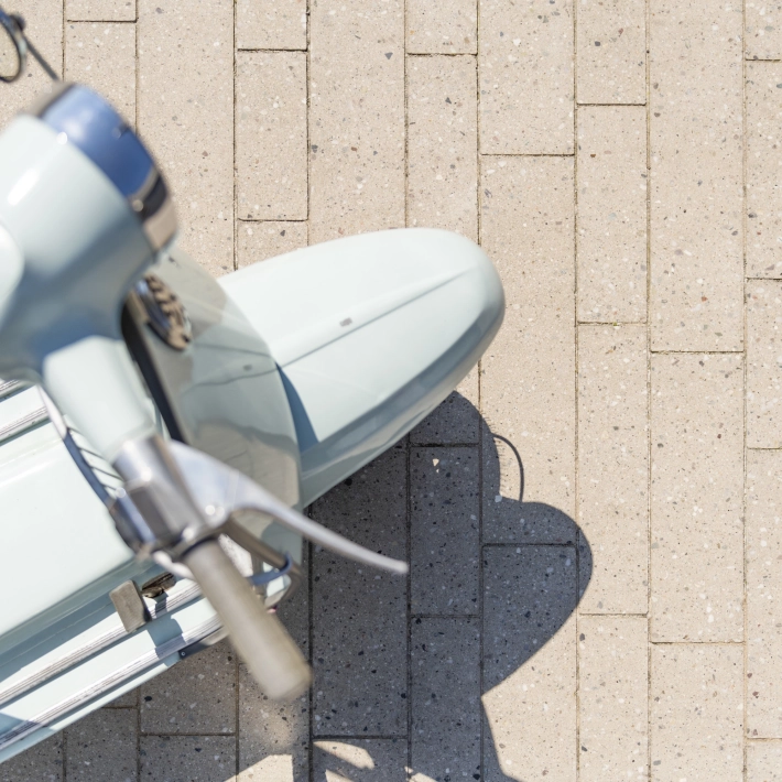 Draufischt auf eine himmelblaue Vespa auf einer geplasterten Fläche mit 
Terrazzo-Steinen mit sichtbarer Körnung Format eines Stabparkets.