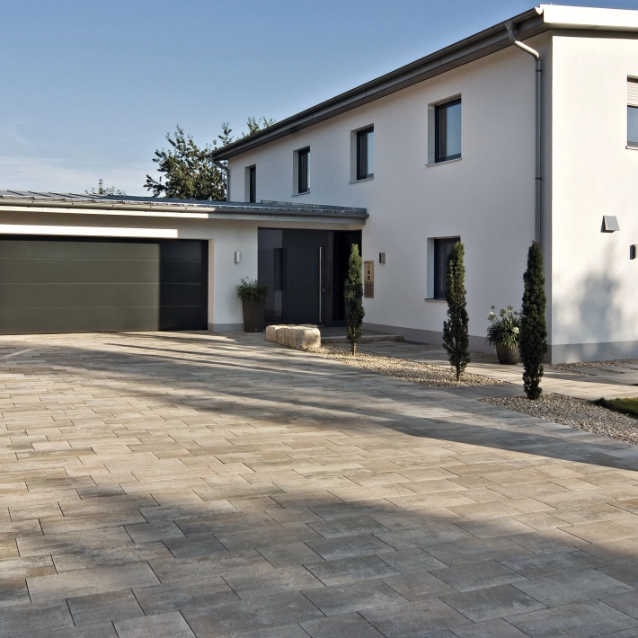 Driveway of a detached house with garage and plants on a private property.