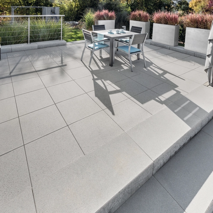 Large terrace with gray patio slabs and steps surrounded by planters.