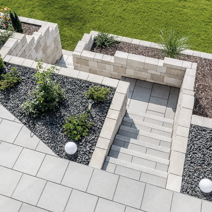 Terrasse mit Treppenabgang aus Betonstein und Terrasiertem Hang abgestützt mit einer Naturstein mauer  und angelegten udn bepflanzten Beeten.<br>