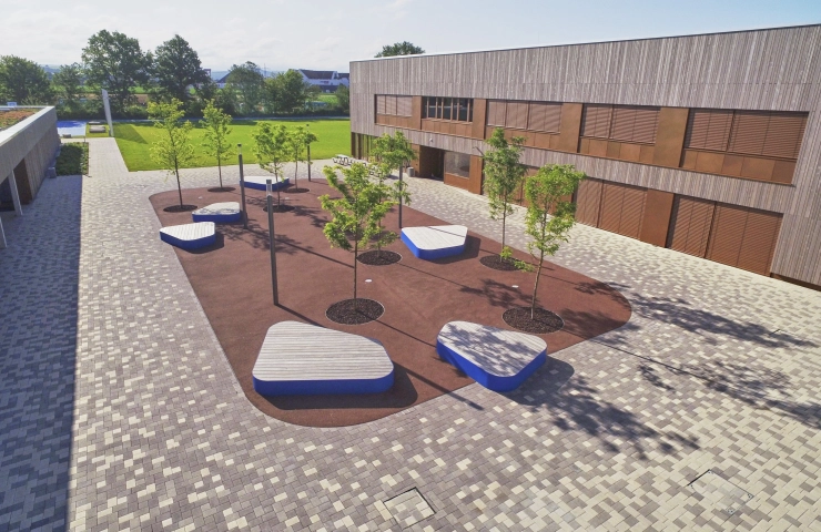 Luftbild mit Blick in den modernen Schulhof: Von hellem bis zu dunklem Braun – drei harmonisch aufeinander abgestimmte Farbtöne setzen die Freianlagen der Realschule Hirschaid im Landkreis Bamberg wirkungsvoll in Szene.