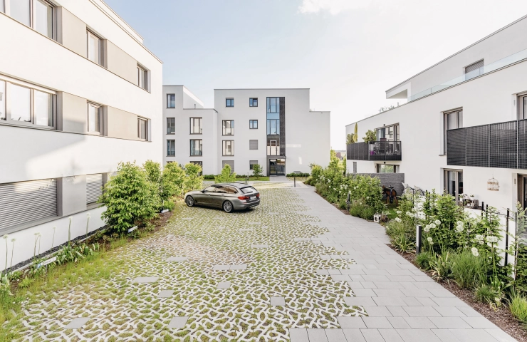 Parkplatzfläche eines Wohnquartiers mit begrünten Pflastersteinen, vom Typ GDM. SCADA ornament, auf denen ein Auto parkt.