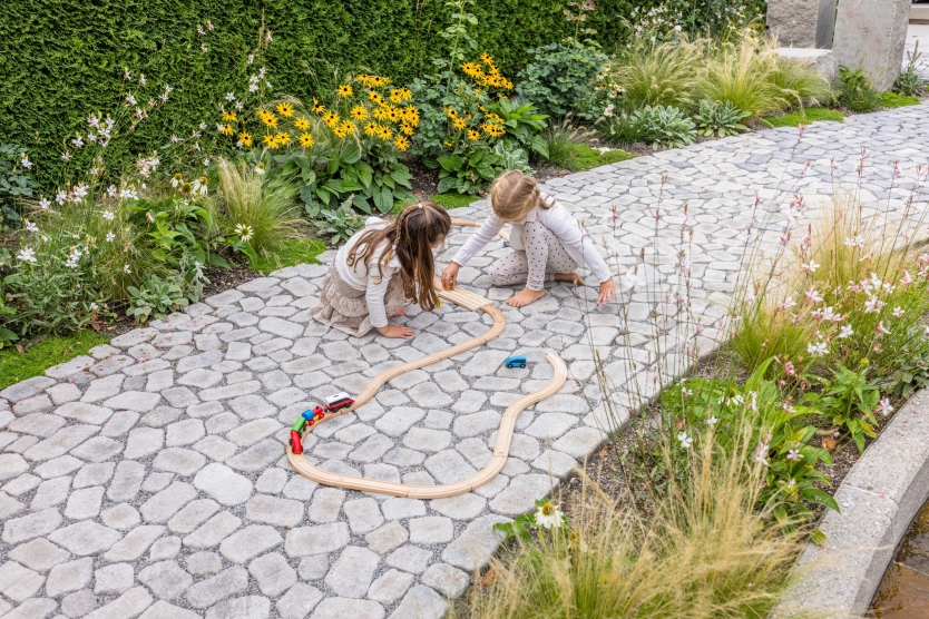 Zwei Mädchen spielen mit einer Holzeisenbahn auf einem Gartenweg mit GODELMANN Pflaster